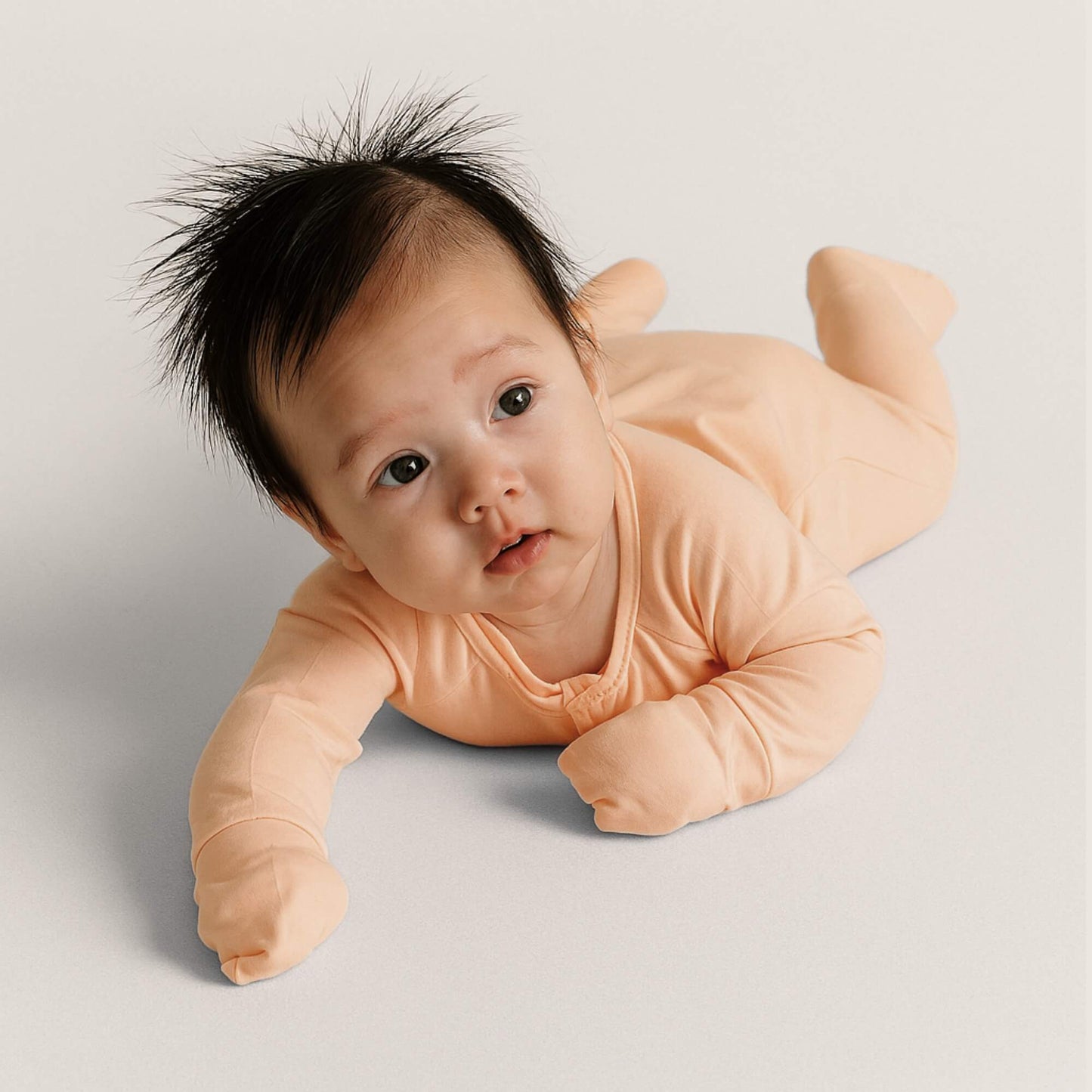 Baby in a peach onesie lying on a light gray background