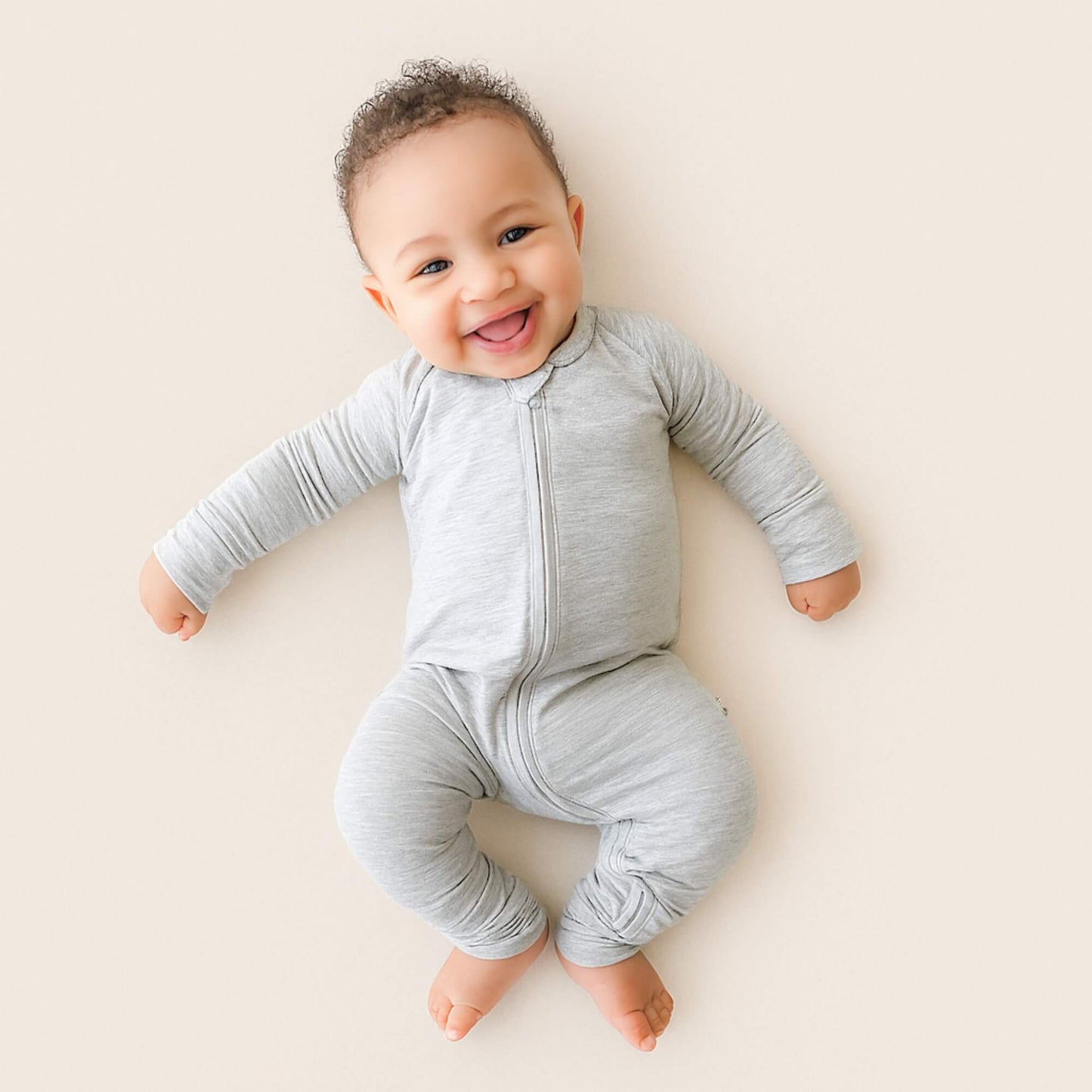 Baby wearing a gray onesie on a light beige background