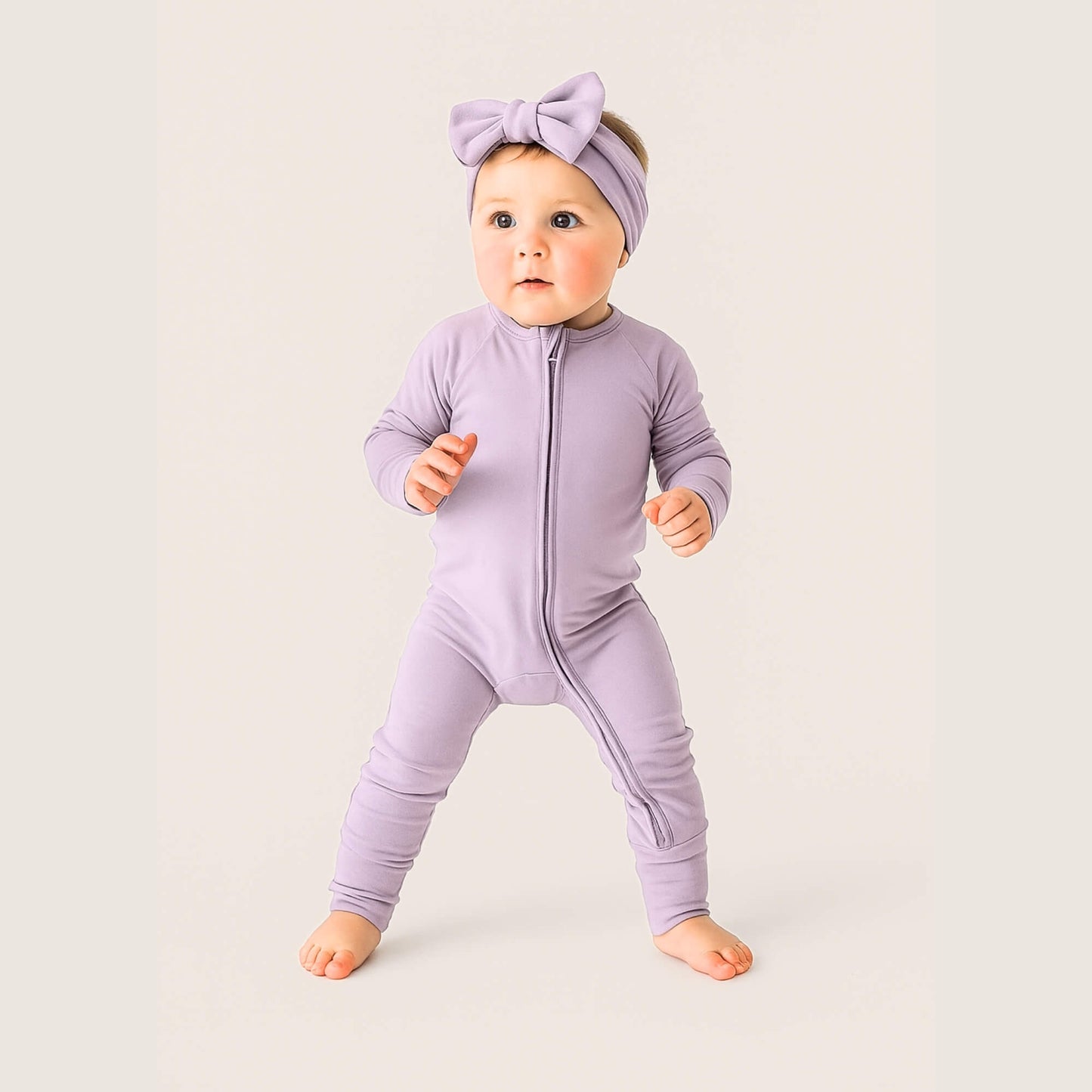 Baby wearing a purple onesie and headband on a light background