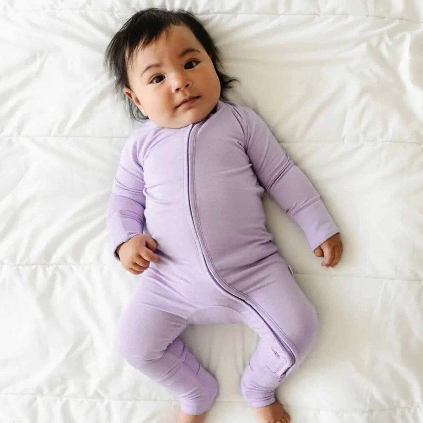 Baby wearing a purple onesie lying on a white surface