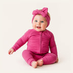 Baby in a pink outfit with a matching headband on a light background