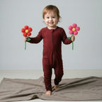 Toddler wearing a maroon bamboo baby grow holding flowers