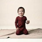 Toddler wearing a maroon bamboo baby grow sitting