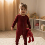Toddler wearing a maroon bamboo baby grow standing in room