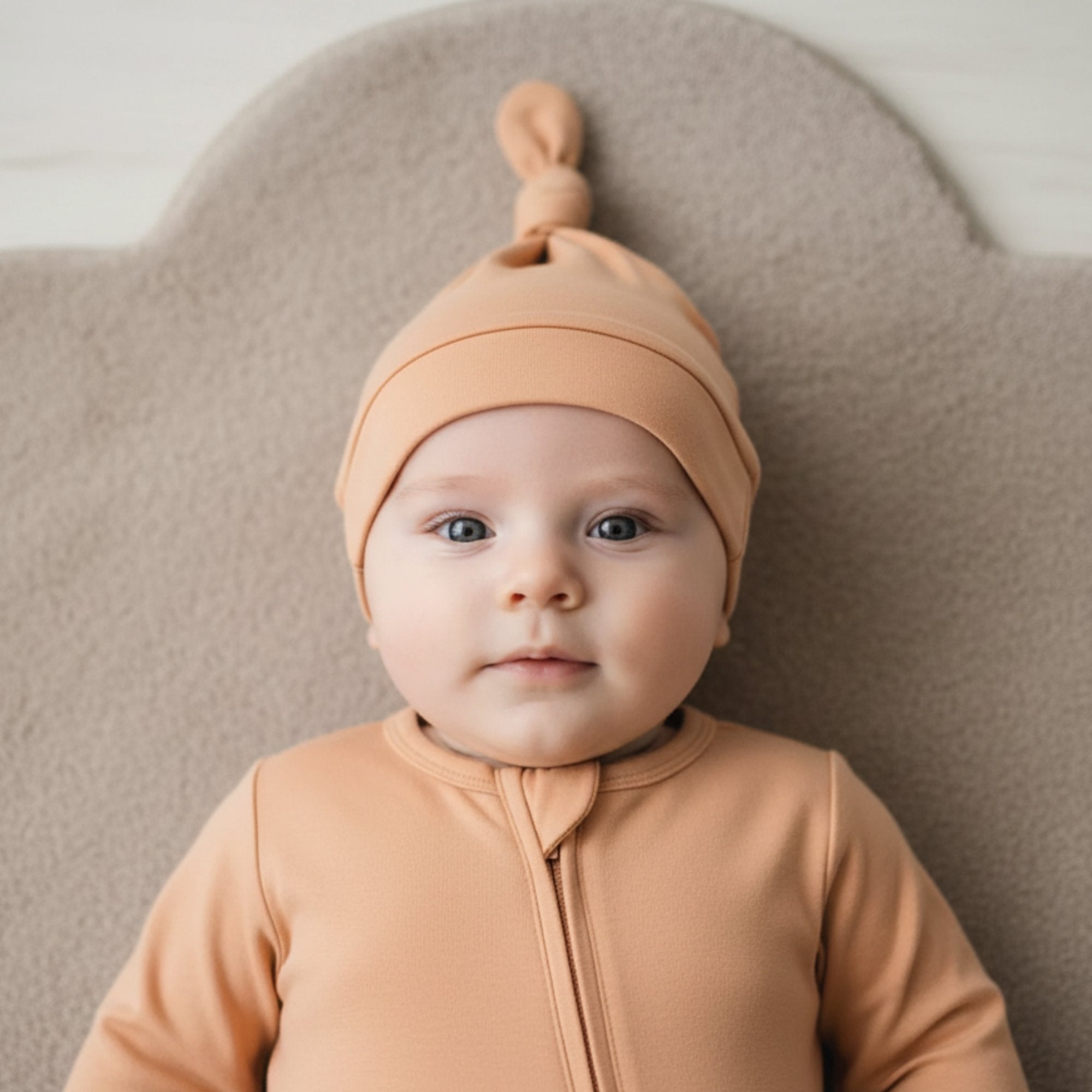 Baby in a orange outfit and hat sitting on a white surface