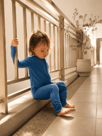 Toddler wearing deep blue bamboo baby grow leaning on balcony