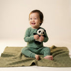 Baby in green bamboo baby grow holding a panda toy