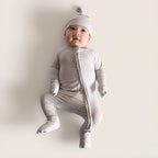 Baby in a light grey baby grow with a matching hat on