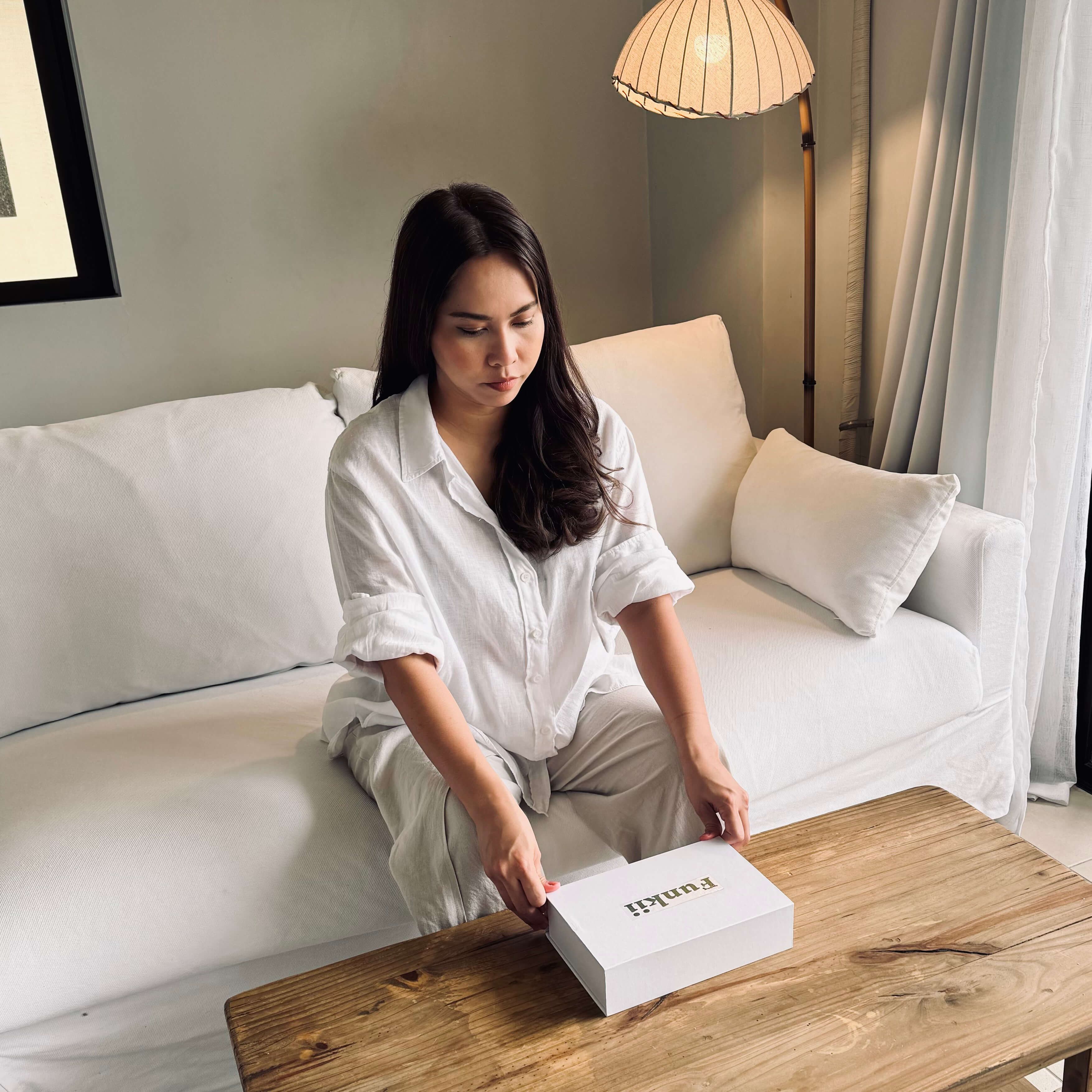 Woman opening a box on a wooden table in a living room.