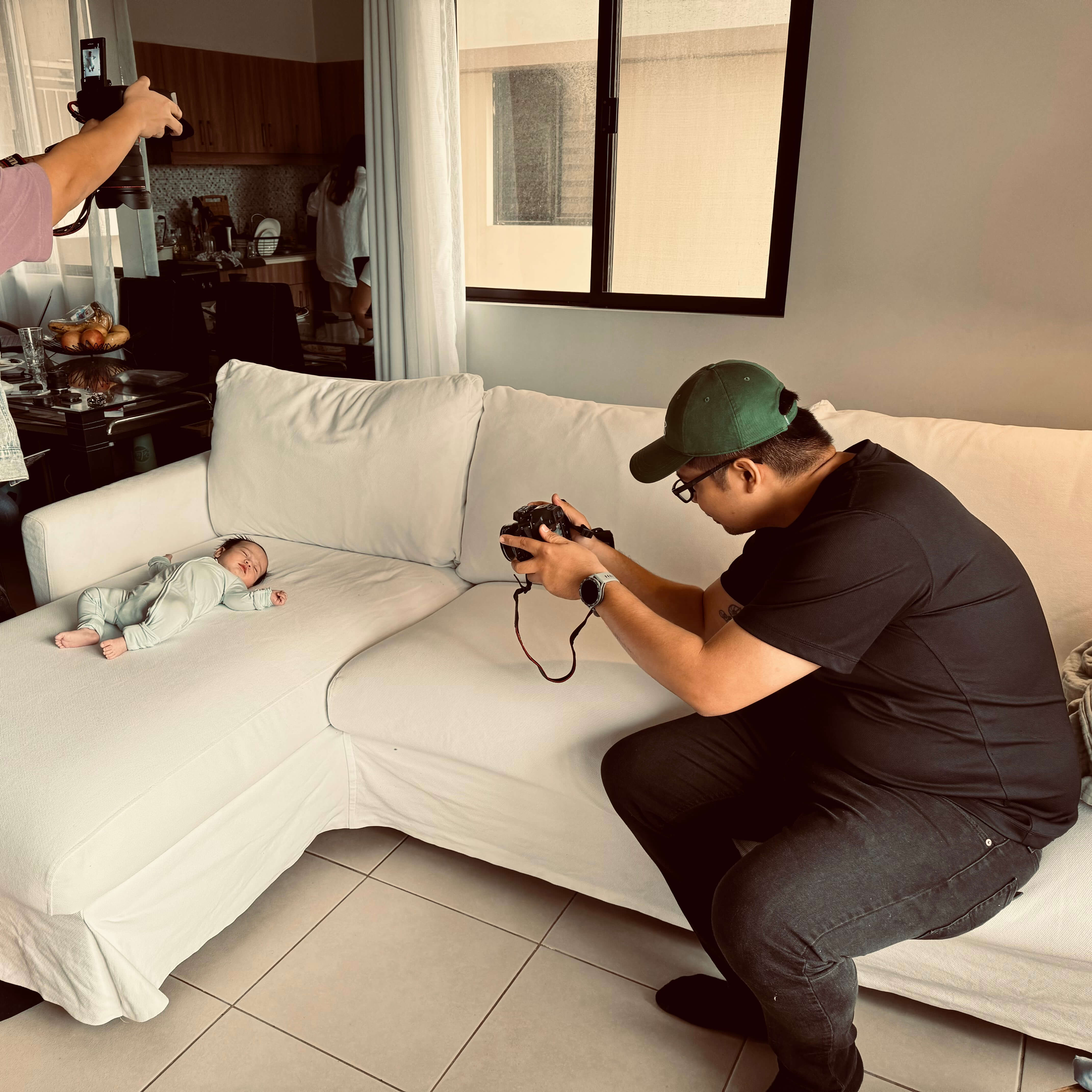 Man taking a photo of a baby on a white couch in a living room.