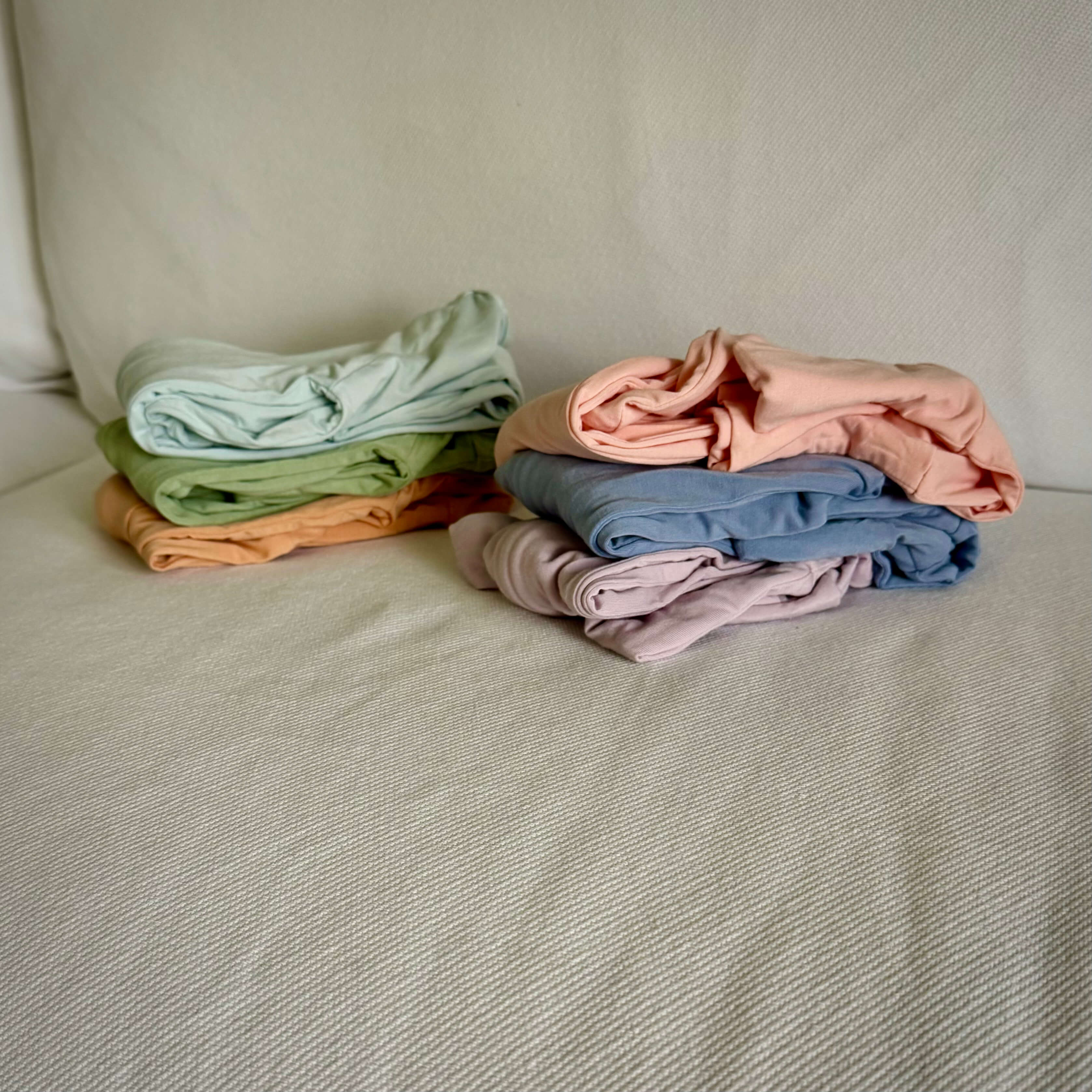 Stacks of folded baby grows in pastel colours on a neutral background