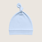 Light blue baby hat with a knot on top against a beige background