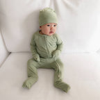 Baby in a green outfit with a matching hat, laying on grey blanket