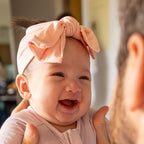 Baby with a pink bow headband being held by an adult
