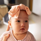 Baby wearing a pink headband with a bow, looking directly at the camera.