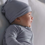 Baby wearing a blue hat and outfit, lying on a soft surface.