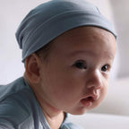 Baby wearing a light blue knotted hat against a neutral background
