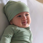 Baby wearing a green outfit and headscarf, smiling.