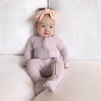 Baby wearing a lavender pyjamas sitting on sofa