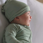 Baby wearing a green pyjamas and hat laying down