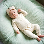 Newborn laying in off white babygrow and bow