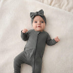 Baby in a grey bamboo babygrow and headband lying on a beige blanket
