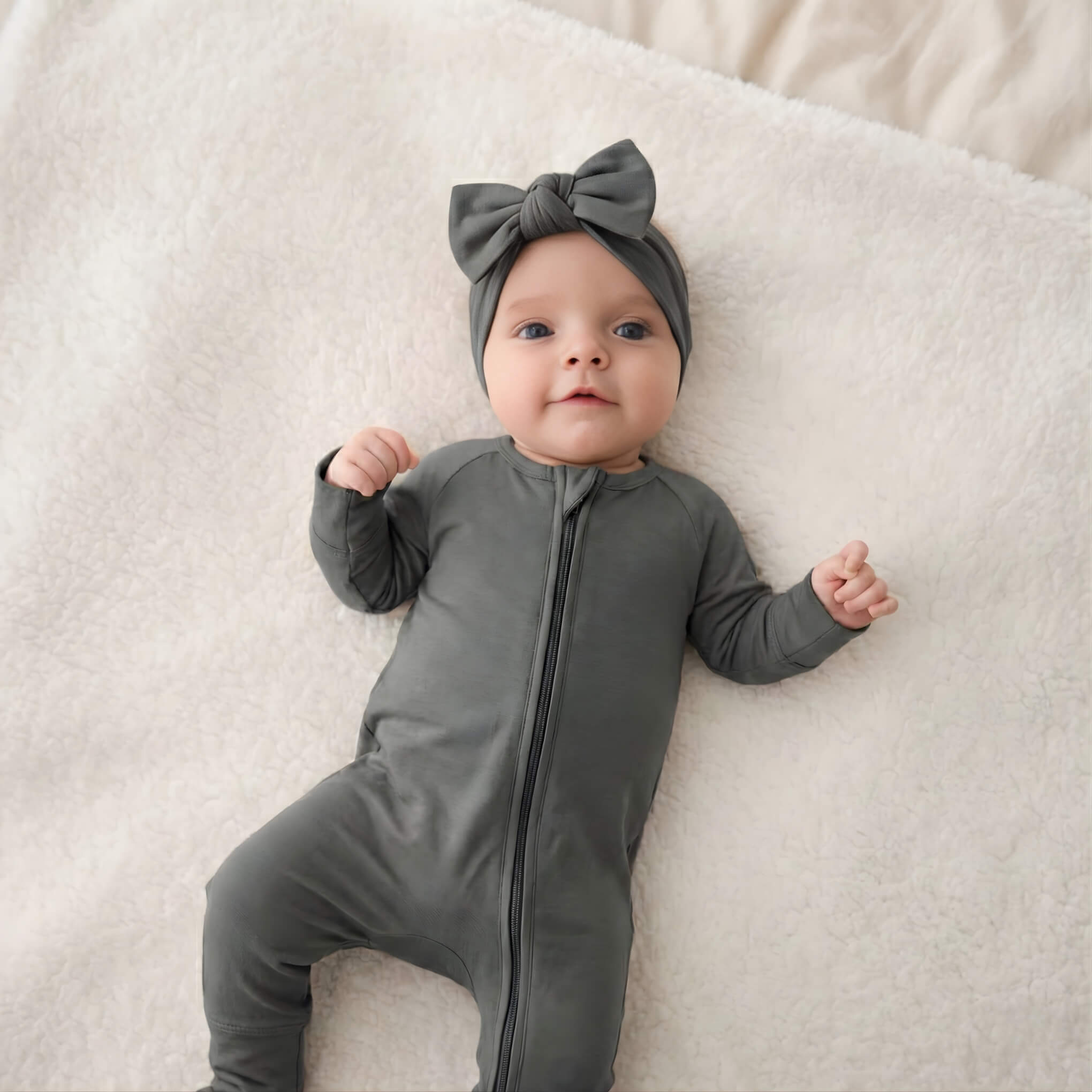 Baby in a grey bamboo babygrow and headband lying on a beige blanket