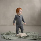 Child in a grey bamboo baby grow standing on a textured green blanket