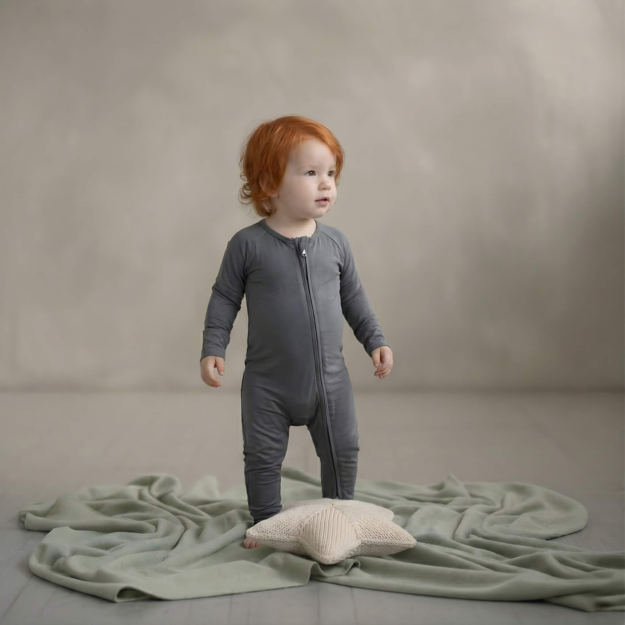 Child in a grey bamboo baby grow standing on a textured green blanket