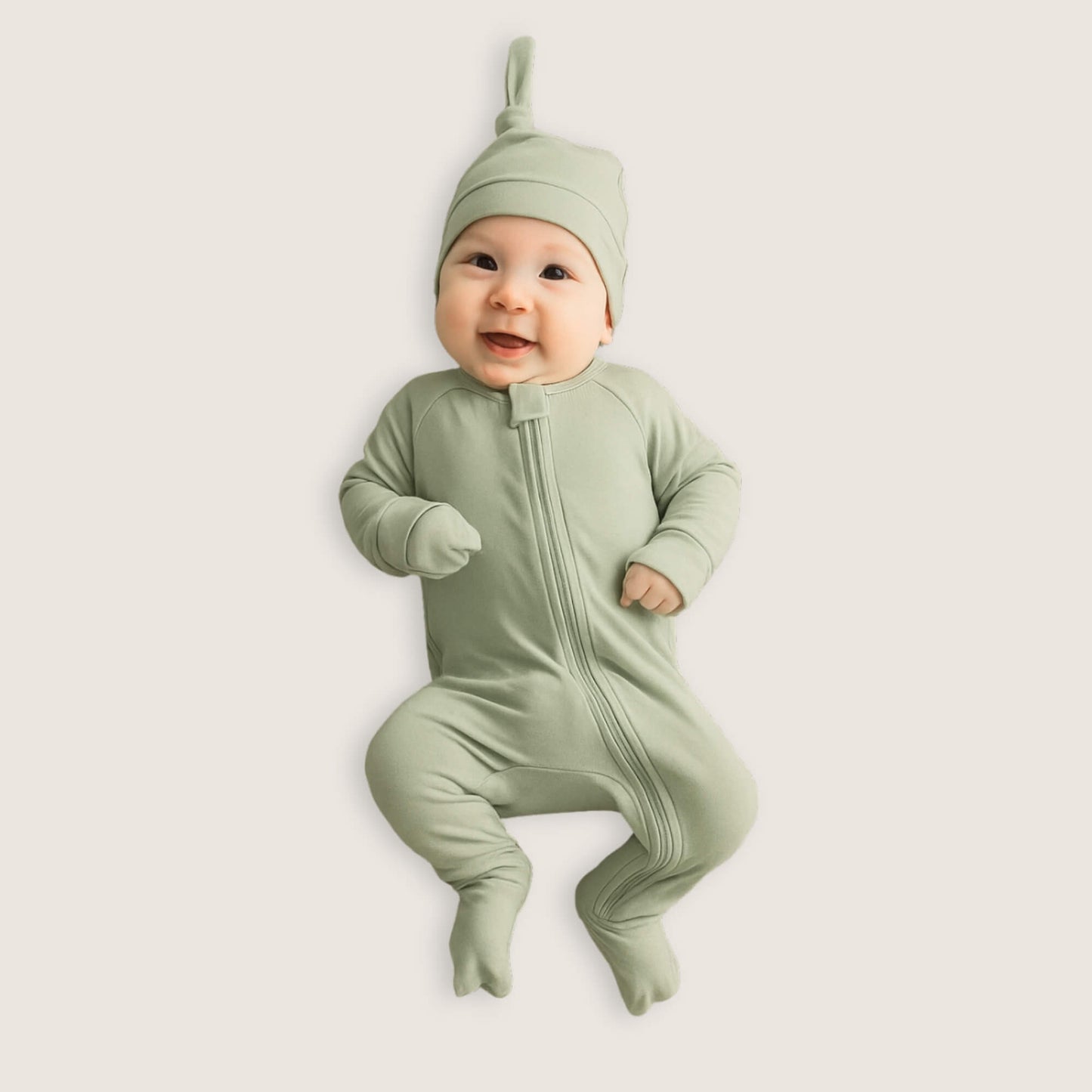 Baby wearing a green pyjamas and hat on a light background