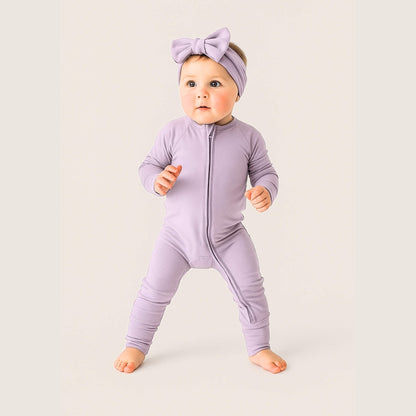 Baby wearing a purple onesie and headband on a light background
