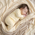 Newborn wearing yellow baby grow sleeping wrapped in blanket