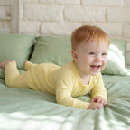 Toddler wearing yellow baby grow laying on bed