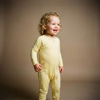 Toddler wearing yellow baby grow standing smilling
