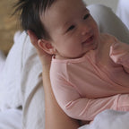 Baby wearing pink pyjama playing in mums arms